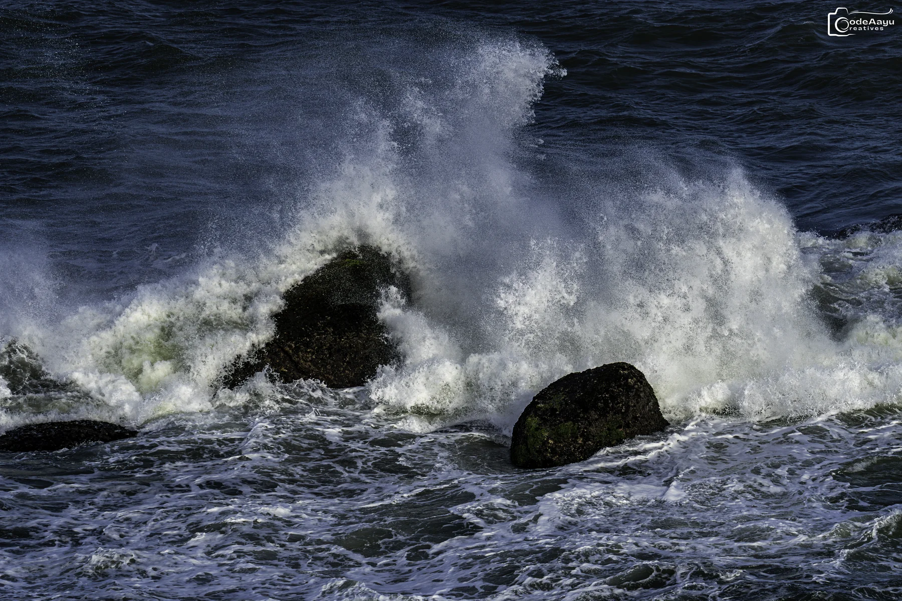 Large ocean wave breaking against dark rocks